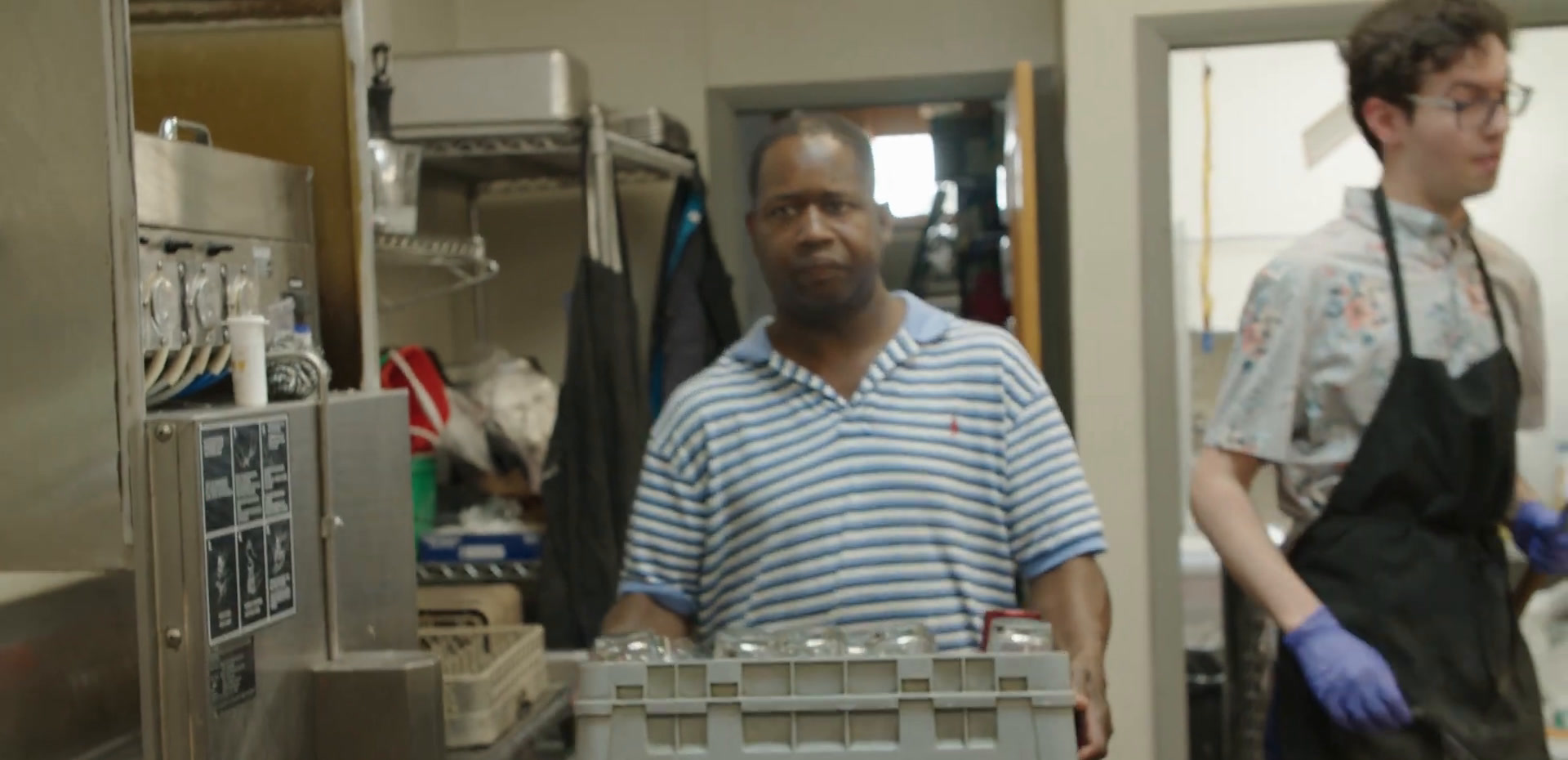 Aaron in a striped polo shirt carrying a rack of glassware through the bar area.