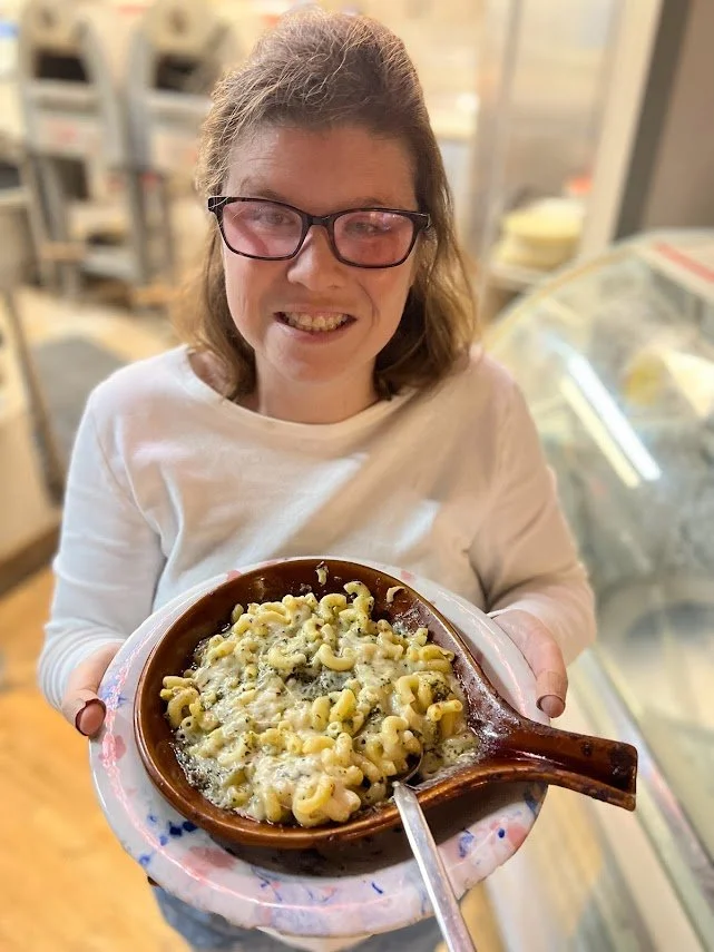 A Brewability team member holding a dish of baked macaroni and cheese, presenting it to the camera.